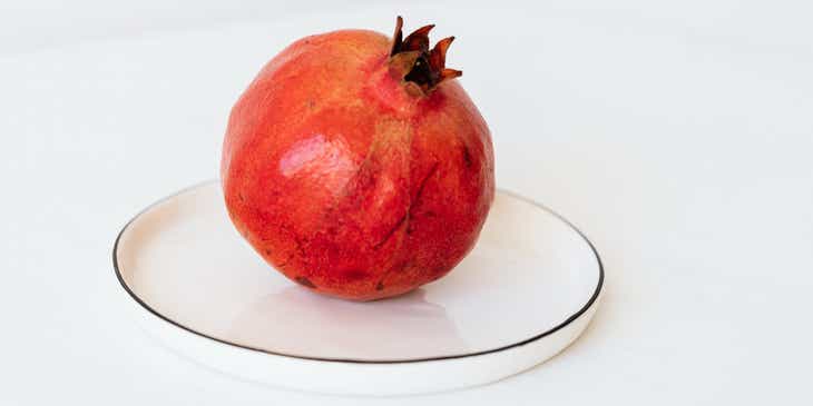 Owoc granatu na białym talerzu, przypominający czerwone koło.