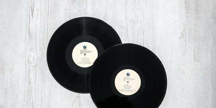 Zwei schwarze Vinyl-Schallplatten als Symbol der Retro-Bewegung liegen auf einer weißen, holzgefaserten Oberfläche.