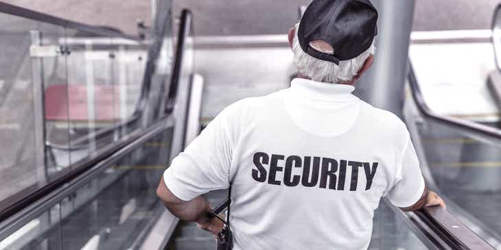 Ein Mitarbeiter einer Sicherheitsfirma steht auf einer Rolltreppe und macht seine Runde in einem Gebäude.