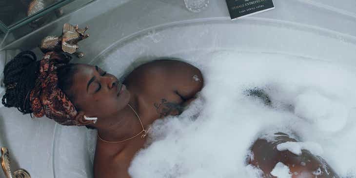 A woman practicing self-care by taking a bubble bath and listening to music.