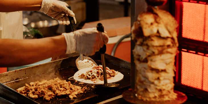 Un hombre sirviendo carne cortada de shawarma del asador.