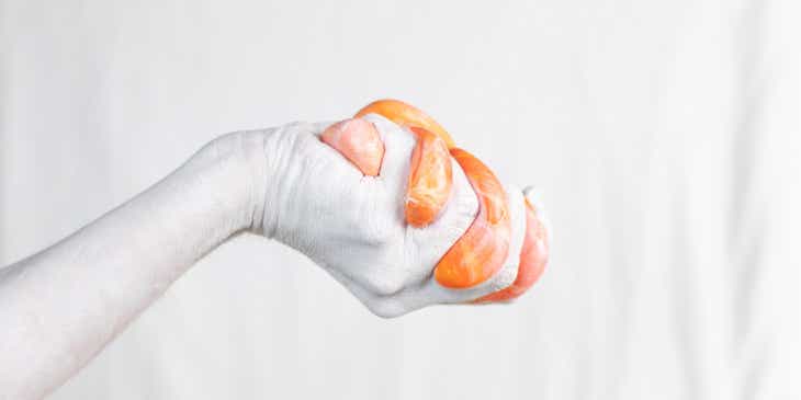 Eine weiß gepuderte Hand quetscht orangen Spielschleim.