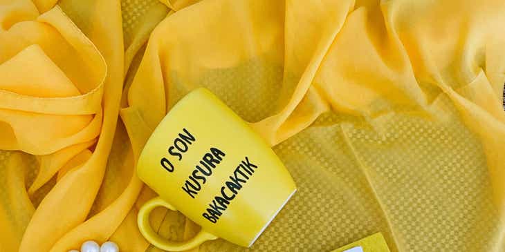 Bir örtünün üzerinde üstünde bir slogan yazan sarı bir kupa bardak.