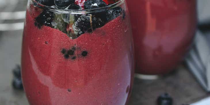 Zwei rote Fruchtsmoothies in Gläsern und mit Erdbeeren und Blaubeeren garniert.