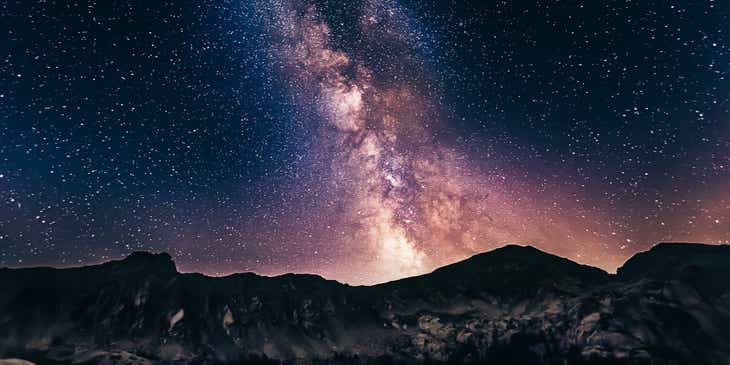 Blick in den Weltraum bei Nacht: Die Milchstraße leuchtet hell oberhalb einer Gebirgskette.