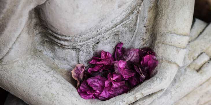 Flores púrpuras en el regazo de una estatua en un negocio de coaching espiritual.