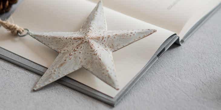 Ein weißer Stern liegt neben einer Kerze und zwei Tannenzapfen auf einem aufgeschlagenen Buch.