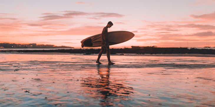 A surfer walks off the beach at sunset.