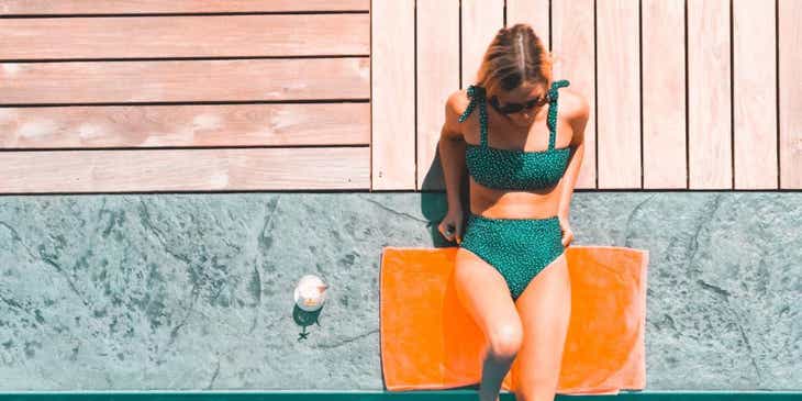 Una donna che sta prendendo il sole in costume sul bordo di una piscina.