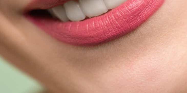 Die obere Zahnreihe einer lächelnden Person ist von gutgepflegten Lippen eingerahmt.