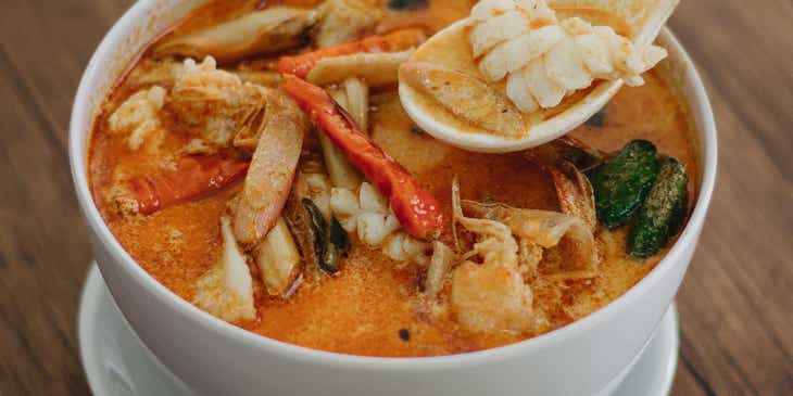 Une soupe thaïlandaise à la noix de coco dans un bol en céramique blanche.