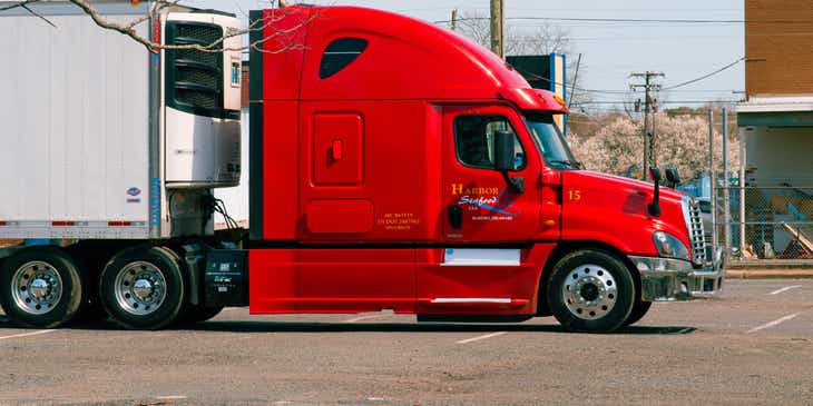 A red and white transportation truck parked at a warehouse.