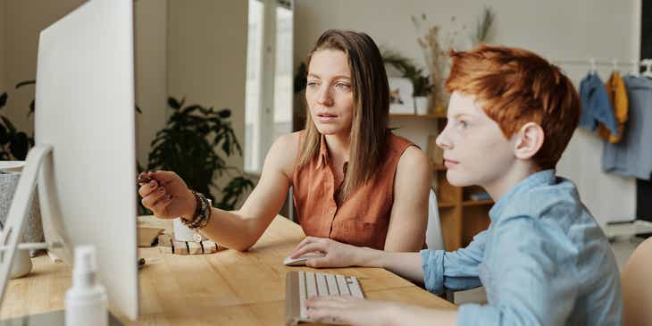 Młoda tutorka udzielająca korepetycji chłopcu przy komputerze.
