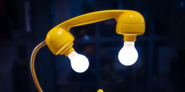 An upcycled yellow rotary phone with protruding light bulbs attached to the receiver.