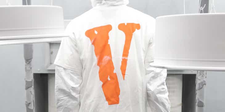 Osoba w białym ubraniu ochronnym z pomarańczową literą „V”.