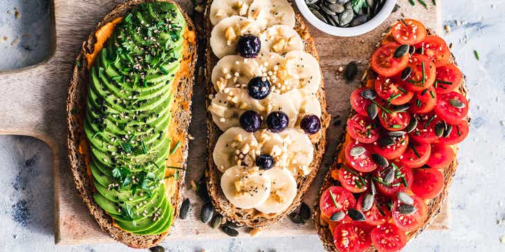 Tres panes tostados con diferentes toppings saludables en un plato de madera en un restaurante vegano.