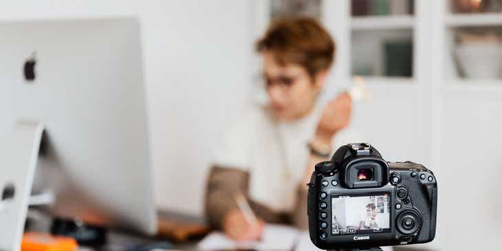 Eine Frau sitzt vor einer Kamera an ihrem Schreibtisch und bereitet Videoinhalte für Ihren Vlog vor.