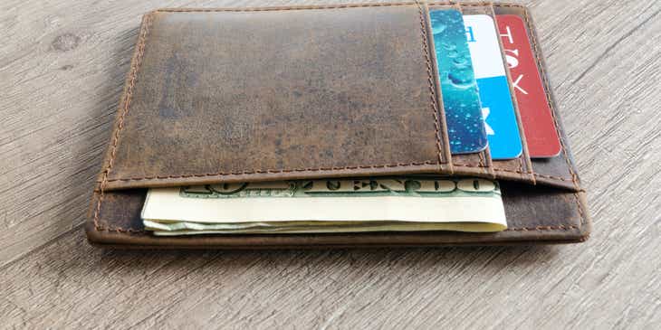 A brown wallet containing credit cards and U.S. dollar bank notes.