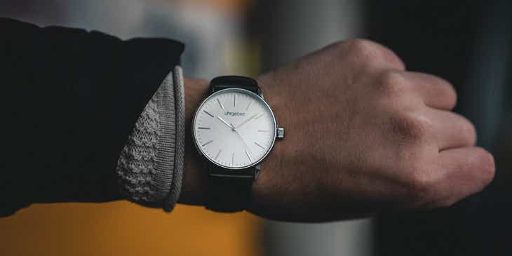 Une personne essaie une montre avec un bracelet en cuir et un cadran blanc.