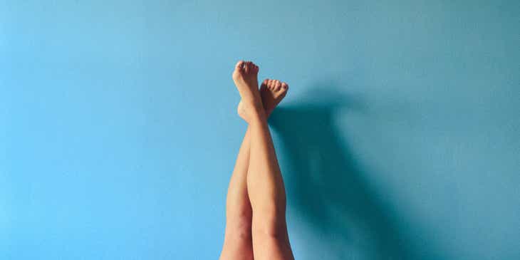 Une paire de jambes fraîchement épilées à la cire appuyées contre un mur bleu.
