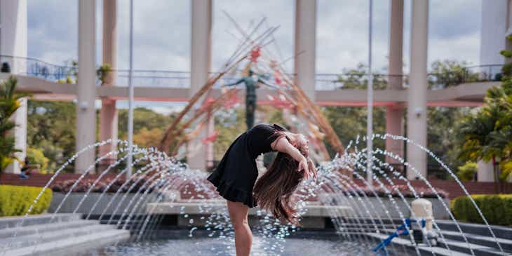 Eine Balletttänzerin posiert vor einem Springbrunnen und einer wunderlichen Statue.