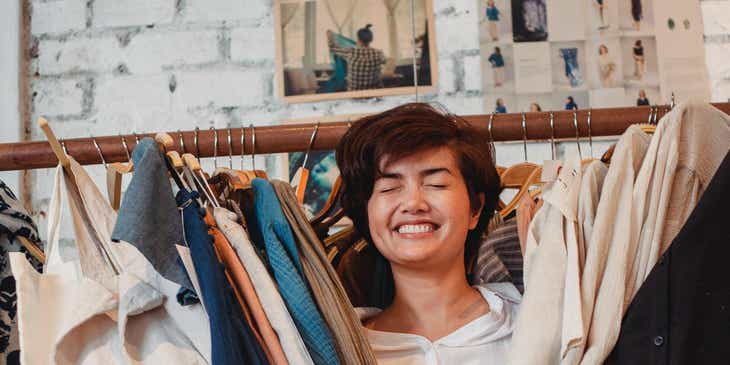 A smiling woman standing between women's clothing on a rack.