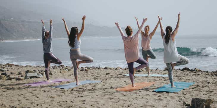 Una mujer saludable haciendo yoga en una playa con su grupo.