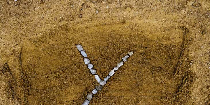 Litera „Y” ułożona z kamyczków na piasku.