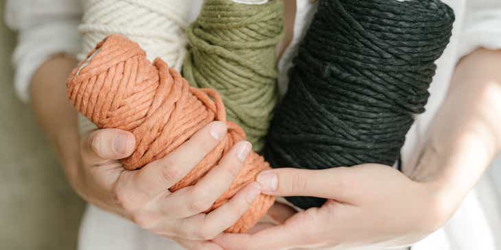 A person holding three colorful yarns.